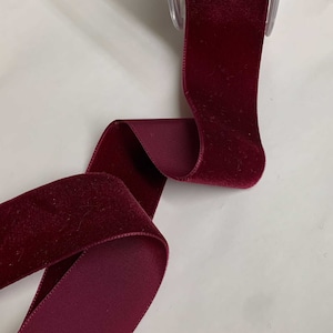 Könnte beinhalten: Eine Rolle tiefrotes Samtband. Das Band ist weich und luxuriös und perfekt, um jedem Projekt einen Hauch von Eleganz zu verleihen.