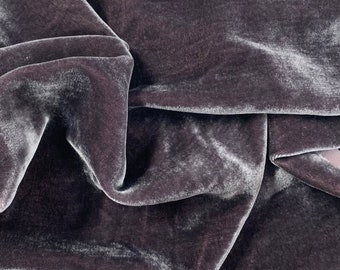 May include: Close-up of a soft, dark gray velvet fabric with a subtle sheen. The fabric is draped and folded, showcasing its texture and drape.