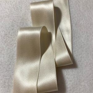 May include: A roll of ivory satin ribbon. The ribbon is smooth and shiny, with a subtle sheen.