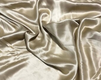Puede incluir: Una tela suave y sedosa de color beige claro. La tela está drapeada y doblada, mostrando su textura lujosa.
