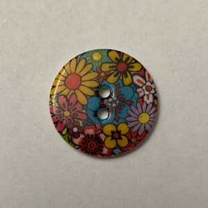 May include: A colorful button with a floral pattern. The button has two holes and is made of plastic.