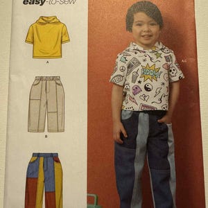 May include: Simplicity sewing pattern R12145 for children's clothing. The pattern includes a short-sleeved hooded shirt and trousers. The image shows a child wearing the outfit. The pattern is designed and printed in the USA.