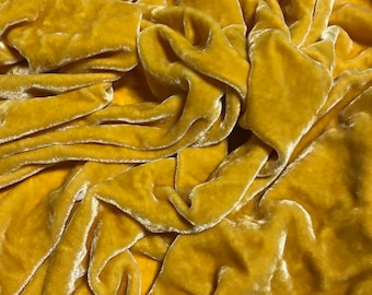 May include: A close-up of a soft, yellow velvet fabric. The fabric is draped and folded, showing its texture and sheen.