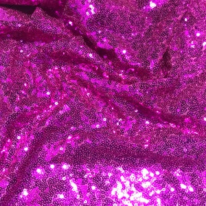 May include: A close-up of a fabric with a bright magenta color, covered in small, shiny sequins.