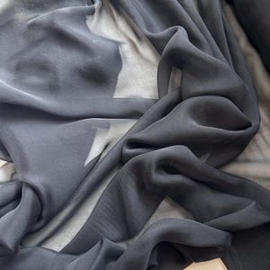 May include: Black sheer fabric with a soft, flowing texture. The fabric is draped and folded, showcasing its delicate and translucent quality.