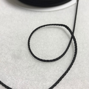 May include: A spool of black waxed cord, with a length of cord extending from the spool.