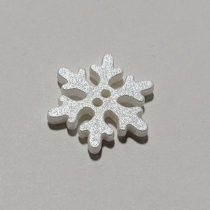 May include: A white snowflake-shaped button with a glittery finish.