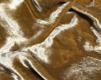 May include: Close-up of a soft, luxurious, gold velvet fabric with a subtle sheen. The fabric is draped and folded, showcasing its texture and drape.