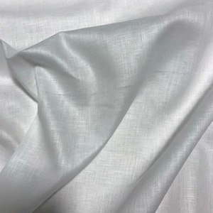 Puede incluir: Primer plano de tela de lino blanca con textura y pliegues visibles. La tela parece suave y ligeramente transl&uacute;cida, con un brillo sutil. La imagen resalta el tejido natural y la ca&iacute;da del material, adecuado para ropa o decoraci&oacute;n del hogar.