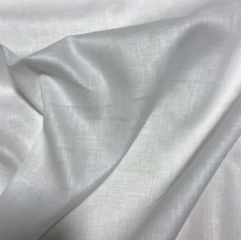 Puede incluir: Primer plano de tela de lino blanca con textura y pliegues visibles. La tela parece suave y ligeramente transl&uacute;cida, con un brillo sutil. La imagen resalta el tejido natural y la ca&iacute;da del material, adecuado para ropa o decoraci&oacute;n del hogar.