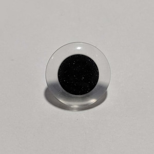 May include: A clear plastic googly eye with a black pupil. The eye is round and has a raised rim.