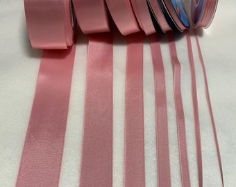 May include: Assortment of pink satin ribbon spools in various widths. The ribbon is smooth and shiny with a subtle sheen.