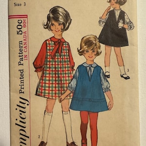 Könnte beinhalten: Vintage Simplicity Schnittmuster für ein Kinderkleid in Größe 3. Das Schnittmustercover zeigt Illustrationen von drei jungen Mädchen in Kleidern. Das Cover ist beige mit rotem und schwarzem Text, einschließlich der Schnittmusternummer und des Preises.