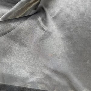 May include: A close-up of a silver sheer fabric with a black trim. The fabric is soft and flowing, with a subtle sheen.