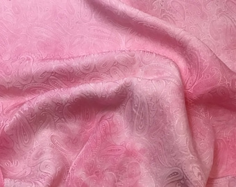 May include: Pink paisley patterned fabric with a soft, silky texture. The fabric is draped and folded, showcasing the intricate design.