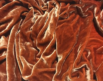 May include: A close-up of a rust-coloured velvet fabric, showing the soft, plush texture and the way the fabric drapes.