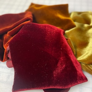 May include: Three pieces of velvet fabric in different shades of red, orange, and yellow. The fabric is soft and luxurious, with a pile that is visible in the image.