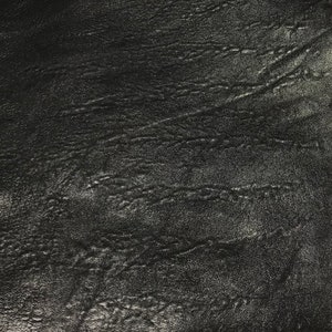 Può includere: Primo piano di una texture in pelle nera con un leggero bagliore. La pelle ha un aspetto leggermente rugoso, creando una superficie testurizzata.