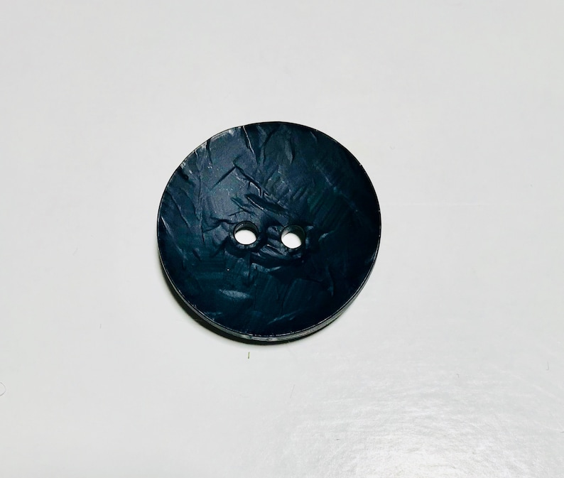 May include: A black button with a textured surface and two holes.