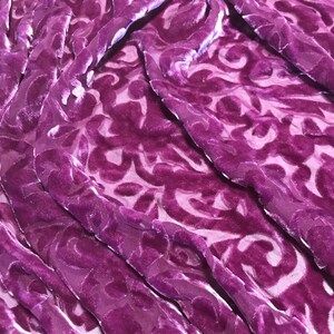 May include: Purple velvet fabric with a damask pattern. The fabric is soft and luxurious, and the pattern is intricate and elegant.