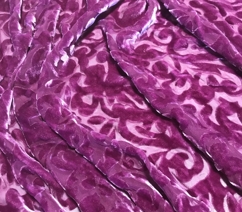 May include: Purple velvet fabric with a damask pattern. The fabric is soft and luxurious, and the pattern is intricate and elegant.