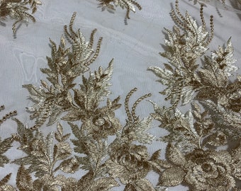 May include: Gold embroidered lace fabric with floral and leaf patterns. The intricate design features raised embroidery, creating a textured and elegant look. The lace is on a sheer white background.