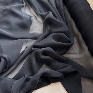May include: Black sheer fabric, a lightweight and translucent material, draped and folded to show its texture.