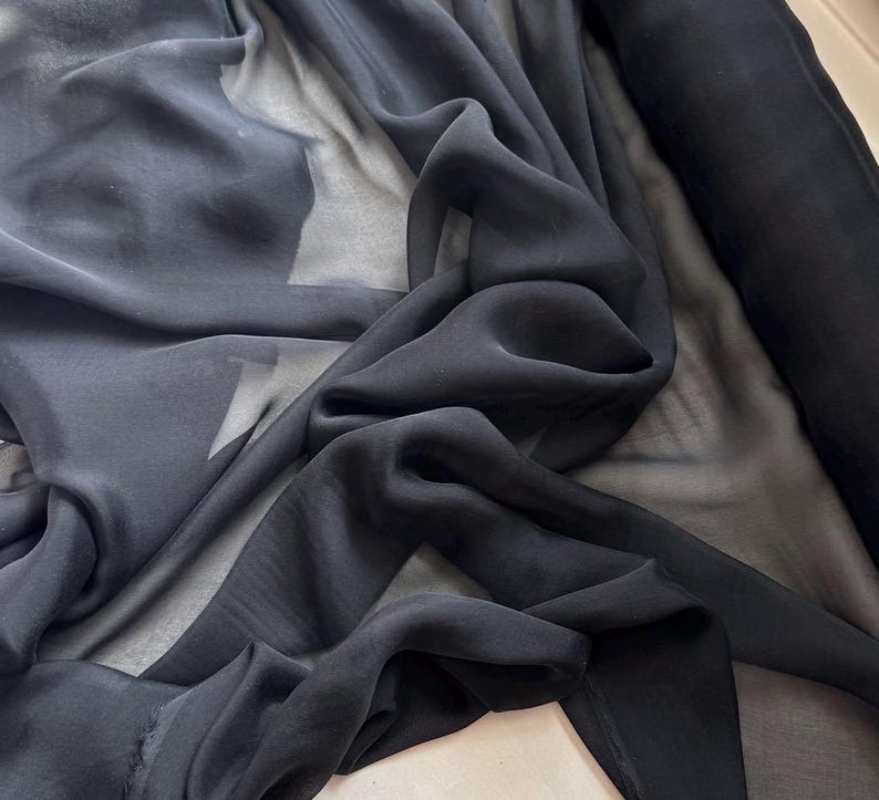 May include: Black sheer fabric, a lightweight and translucent material, draped and folded to show its texture.