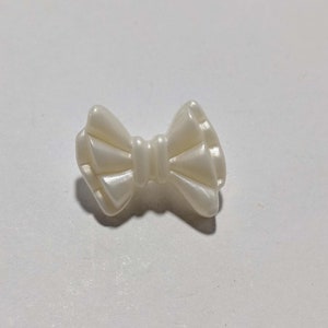 May include: A white plastic bow-shaped button with a textured surface.