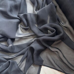 May include: Black sheer fabric with a smooth, silky texture. The fabric is draped and folded, showcasing its transparency and flowy nature.