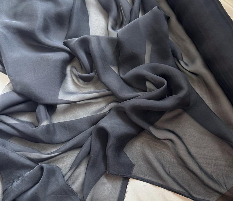 May include: Black sheer fabric with a smooth, silky texture. The fabric is draped and folded, showcasing its transparency and flowy nature.