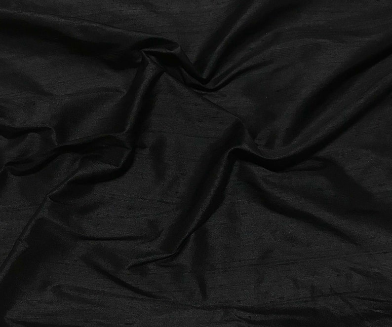 Puede incluir: Tela de seda negra con una textura lisa y brillante. La tela est&aacute; drapeada y doblada, mostrando su calidad suave y fluida.