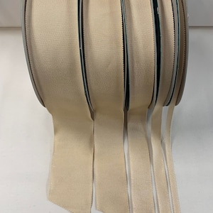 May include: Five spools of beige grosgrain ribbon in various widths. The ribbon is rolled and the ends are hanging down.