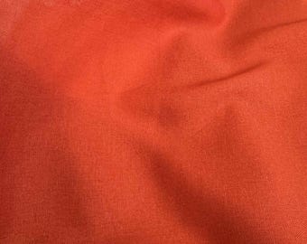 Op de afbeelding: Close-up van een helder oranje stof met zichtbare textuur en subtiele kleurvariaties. Het materiaal lijkt zacht en vloeiend, met zachte plooien en schaduwen die diepte aan het beeld toevoegen. De algemene indruk is van een glad, hoogwaardig textiel.