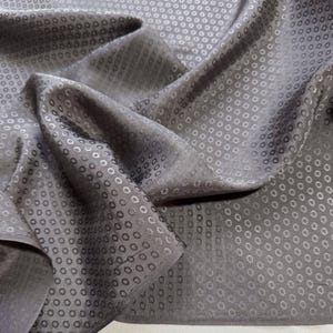 Puede incluir: Primer plano de una tela gris con un sutil patrón en relieve de pequeños círculos. La tela está doblada y drapeada, mostrando su textura y caída.