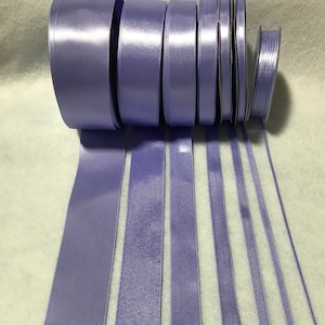 May include: A set of lavender satin ribbon rolls in various widths. The rolls are arranged in a row, with the widest roll at the top and the narrowest roll at the bottom.