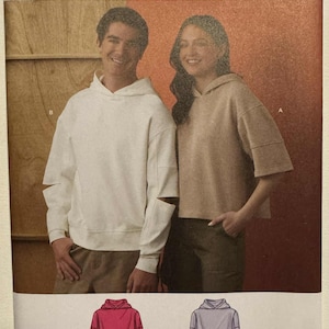 Puede incluir: Patrón de costura Simplicity para una sudadera con capucha y mangas recortadas. Incluye tallas XS-XXL. La imagen muestra a un hombre y una mujer con la sudadera en blanco y beige. El patrón es fácil de coser.