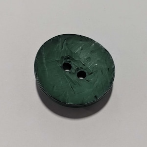 May include: A dark green, two-hole button with a textured surface.