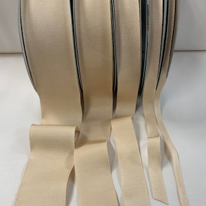 May include: Five spools of beige grosgrain ribbon in various widths. The ribbon is smooth and has a subtle sheen.