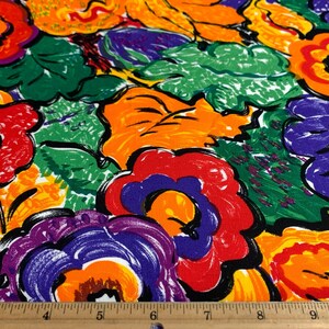 May include: Close-up of a fabric with a vibrant floral pattern. The design features large, stylized flowers in shades of red, orange, purple, and yellow, set against green foliage. The fabric is measured with a ruler.