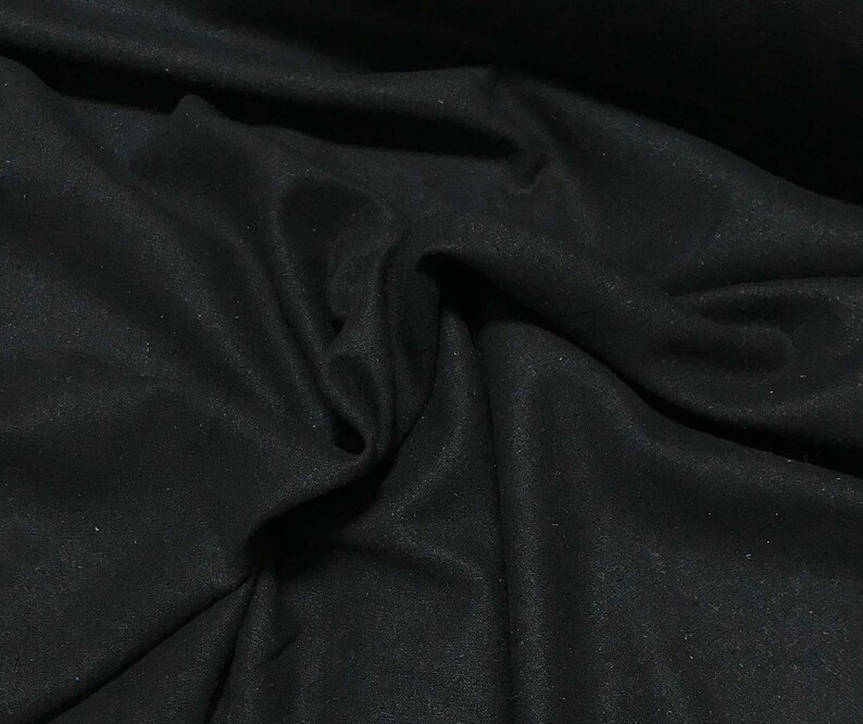 May include: Black fabric with a smooth, slightly textured surface. The fabric is folded and draped, showing its soft and drapey texture.