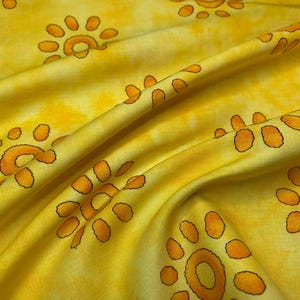 Puede incluir: Tela amarilla con un patrón repetido de soles estilizados en naranja. La tela tiene pliegues suaves y sombras. Los diseños de sol están delineados en un tono naranja más oscuro.