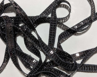 May include: Black sequined trim ribbon. The ribbon is made of a black fabric with silver sequins sewn on in a repeating pattern.