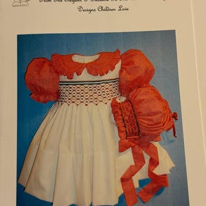 Puede incluir: Un vestido blanco con bordados rojos y verdes, un cuello rojo con volantes y mangas abullonadas. Se incluye un gorro rojo a juego con una cinta blanca. El vestido está etiquetado como "223 ZOEY".