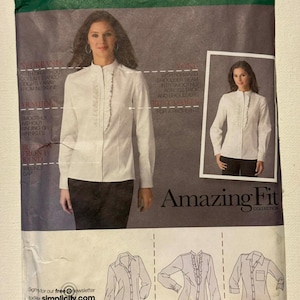 May include: Simplicity sewing pattern featuring a white blouse with a ruffled front. The pattern includes sizes R5 14, 16, 18, 20, and 22. The package also shows a woman wearing the blouse. The text "Amazing Fit Collection" is visible.