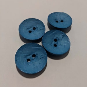 May include: Four blue plastic buttons with two holes each. The buttons have a textured surface and are arranged in a cluster.