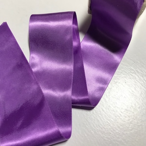 May include: A roll of purple satin ribbon. The ribbon is smooth and shiny, and it is perfect for adding a touch of elegance to any project.