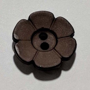 May include: A brown plastic button shaped like a flower with six petals and two holes in the centre.