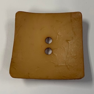 May include: A brown, square-shaped soap dish with two holes in the center.