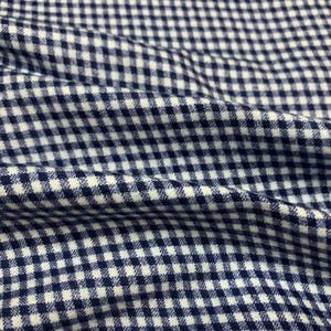 May include: Close-up of a navy blue and white gingham fabric. The fabric is tightly woven, with a repeating pattern of small, evenly spaced squares. The fabric is slightly wrinkled, creating shadows and depth.